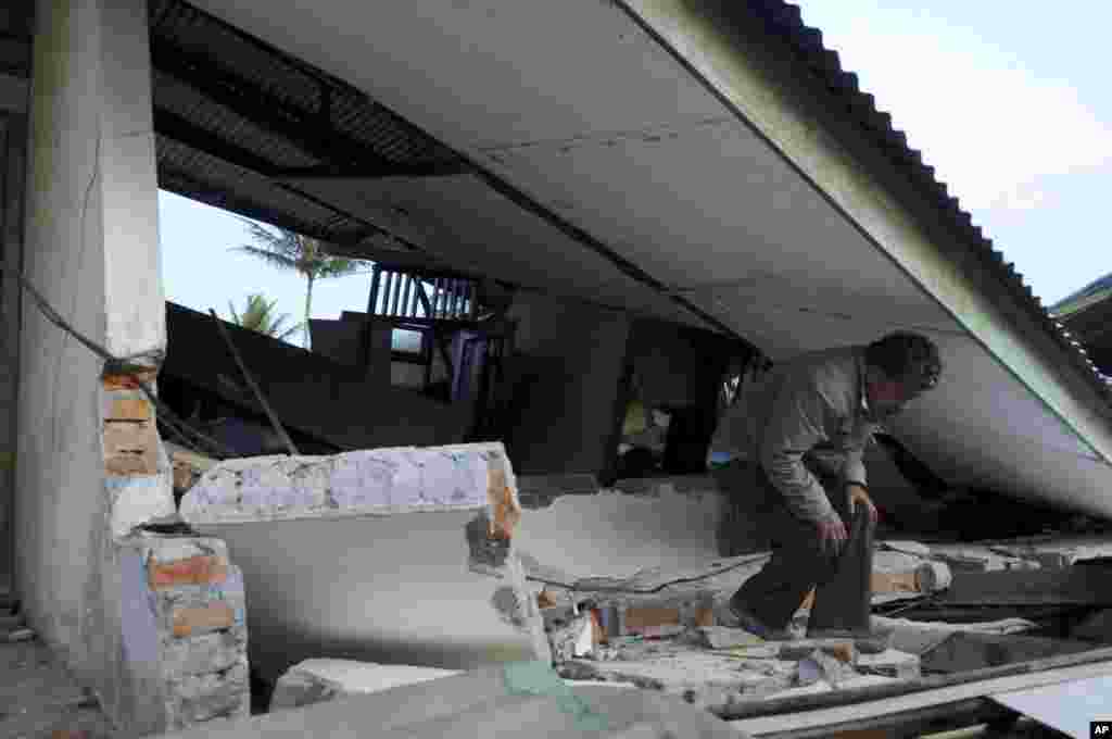 Seorang pria melalui atap sebuah bangunan yang roboh akibat gempa bumi di Ketol, Aceh TEngah (3/7).
