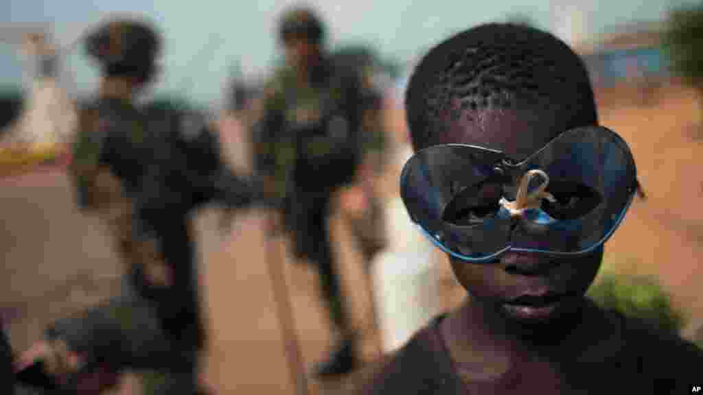 A boy wears a holiday mask as he and other children hang around a group of French soldiers from an armored personnel carrier, posted at an intersection, in Bangui, Central African Republic.