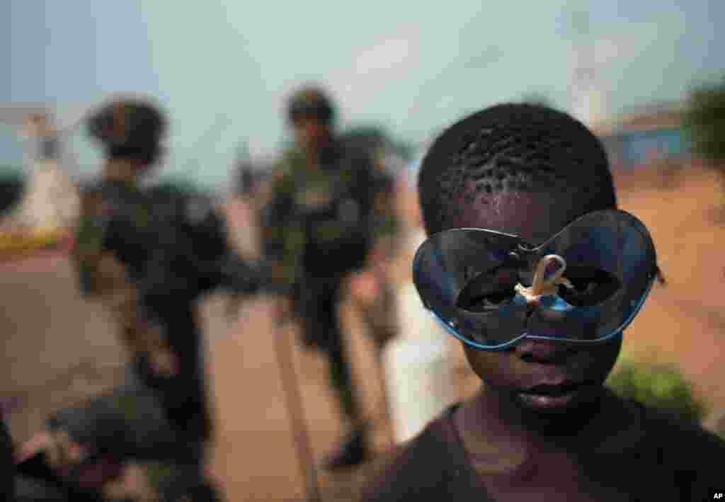 A boy wears a holiday mask as he and other children hang around a group of French soldiers on New Year's Day, Bangui, Central African Republic, Jan. 1, 2014.
