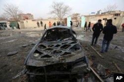 FILE - Afghans gather near a car damaged in Friday's suicide attack in Kabul, Afghanistan, Saturday, Jan. 2, 2016. Taliban spokesman Zabihullah Mujahid claimed responsibility for the attack