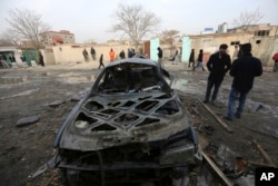 FILE - Afghans gather near a car damaged in Friday's suicide attack in Kabul, Afghanistan, Jan. 2, 2016.