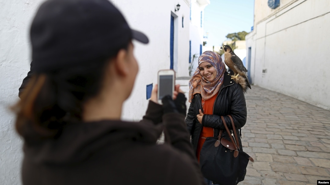 Falconer Maroua (L), for the price of a few dinars, photographs a woman as she poses with a falcon on her shoulder in Sidi Bou Said, a popular tourist destination near Tunis, Tunisia, Feb. 2, 2016.