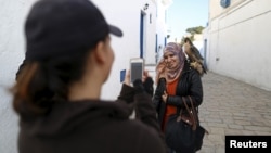 Falconer Maroua (L), for the price of a few dinars, photographs a woman as she poses with a falcon on her shoulder in Sidi Bou Said, a popular tourist destination near Tunis, Tunisia, Feb. 2, 2016.