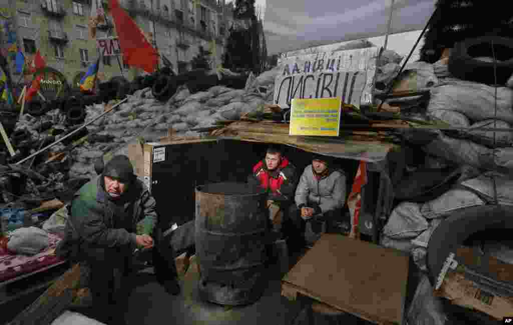 Aktivis pro-Uni Eropa menghangatkan diri duduk di dalam tenda perlindungan di dalam barikade selama protes di Lapangan Kemerdekaan di Kiev, 18 Desember 2013.