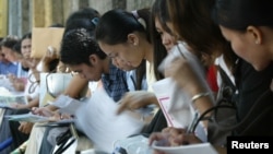 FILE - Young Filipinos fill in forms at a state-organized job fair for outsourcing firms in the Philippines outside the presidential palace in Manila, Oct. 9, 2004. 
