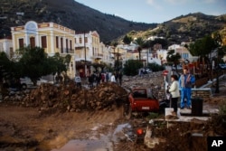 Residents stand next to a damaged road as a washed up vehicle is seen in the background following a powerful storm on the Greek island of Symi, Nov. 14, 2017.