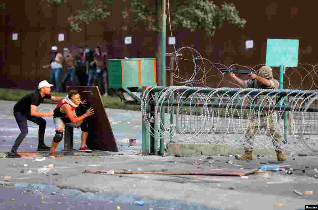 Demonstrators take cover during clashes with security forces during a protest near parliament, as Lebanon marks the one-year anniversary of the explosion in Beirut.