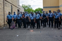 FILE - Minneapolis police officers stand in a line facing protesters demonstrating against the death of George Floyd, outside the 3rd Police Precinct in Minneapolis, Minnesota, May 27, 2020.