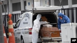 FILE - Funeral workers wearing protective gear as a precaution amid the new coronavirus pandemic push the remains of a COVID-19 victim into a funeral car at a field hospital in Leblon, Rio de Janeiro, Brazil, June 4, 2020. 