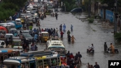 Para pejalan kaki dan pengendara sepeda motor melintasi jalanan yang tergenang banjir akibat hujan lebat di Karachi, Pakistan, 21 Agustus 2020. (Foto: Asif HASSAN / AFP)