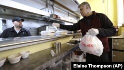 Glen Quadros, owner of the Great American Diner & Bar, checks a takeout order as cook Arturo Aguilar looks on in Seattle.