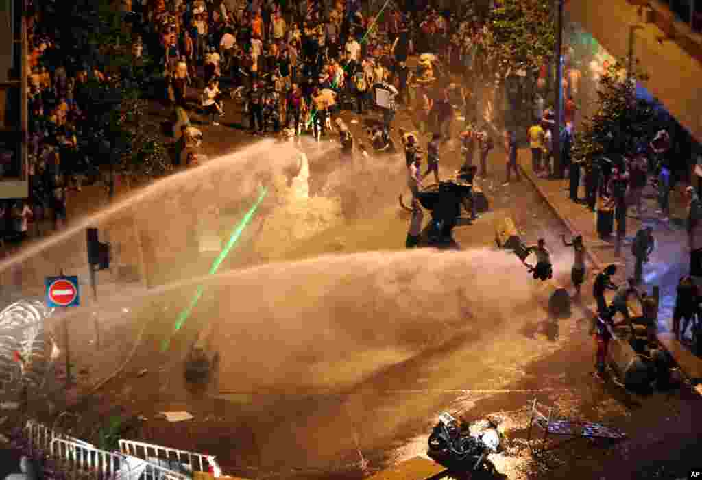 Lebanese activists shout anti-government slogans as they are sprayed by riot police using water cannons during a protest against the ongoing trash crisis, in downtown Beirut, Aug. 23, 2015.