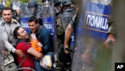 Các di dân giúp người đàn ông giữ một cậu bé bị kẹt giữa cảnh sát chống bạo động Macedonia trong vụ đụng độ hôm 21/8/2015.