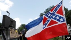Una bandera estatal de Mississippi ondea al lado de un cartel que expresa apoyo a cambiar el diseño frente al Capitolio en Jackson, Mississippi, el 28 de junio de 2020.
