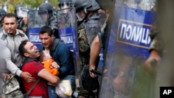 Fellow migrants help a man and boy pressured by Macedonian riot police at the border near Idomeni, northern Greece, Aug. 21, 2015. Migrants hope to cross into Macedonia, which has declared a state of emergency because of the immigrant influx. 