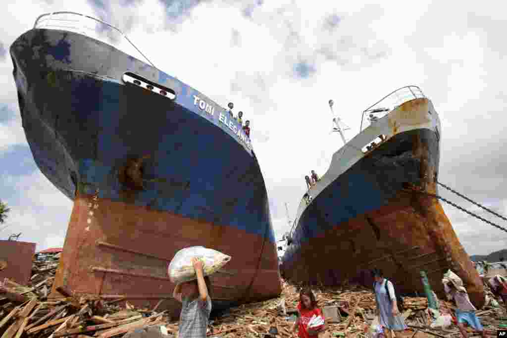 Survivors pass by two large boats that were washed ashore by strong waves caused by Typhoon Haiyan in Tacloban city, Leyte province, central Philippines, Nov. 10, 2013.