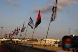 Seorang wanita yang mengenakan masker wajah berjalan melewati bendera Uni Emirat Arab dan Israel di Jembatan Perdamaian di Netanya, Israel, Minggu, 16 Agustus 2020. (Foto: AP)