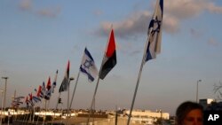 Seorang wanita bermasker berjalan melewati bendera Uni Emirate Arab dan Israel di Jembatan Perdamaian di Netanya, Israel, Minggu, 16 Agustus 2020. (Foto: AP)