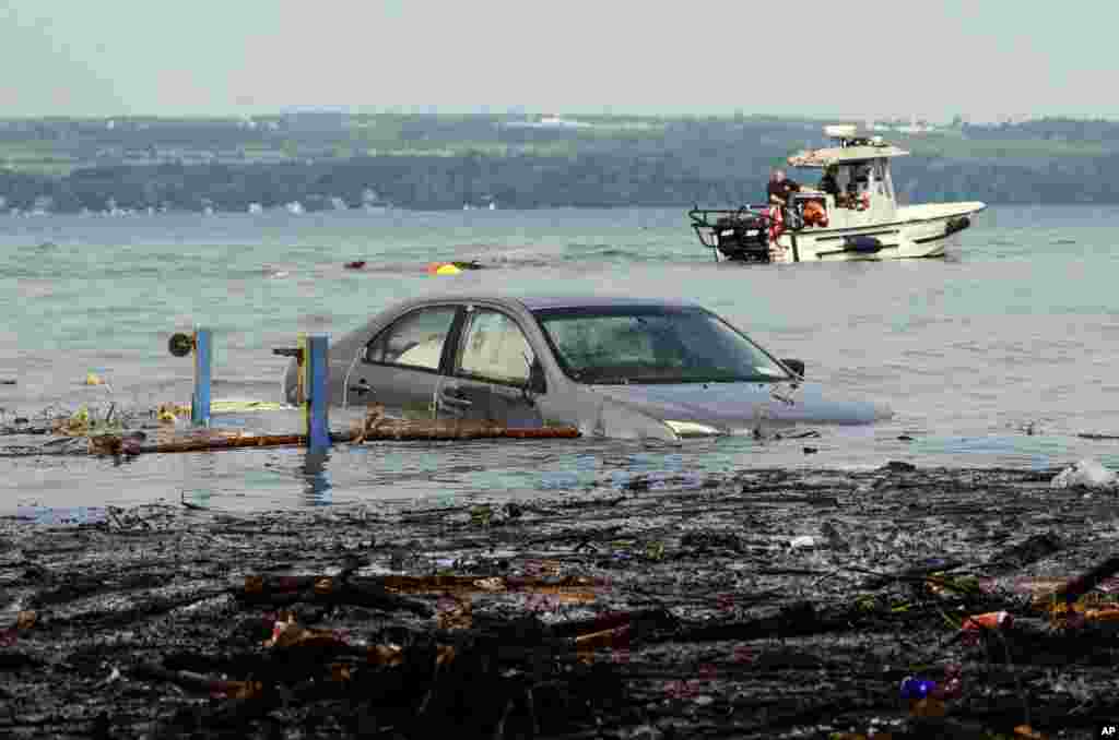 Petugas di atas kapal mencoba menyeret sebuah mobil keluar dari Danau Seneca di Lodi Point, New York, setelah hujan lebat dan banjir bandang melanda kawasan ini.