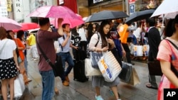 Khách du lịch Trung Quốc chờ xe buýt tham quan ở phía trước của một cửa hàng điện tử giảm giá ở quận Ginza, Tokyo.