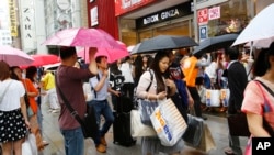 FILE - Chinese tourists with shopping bags await sightseeing bus in front of discount electronics store in Tokyo's Ginza district, June 17, 2015.