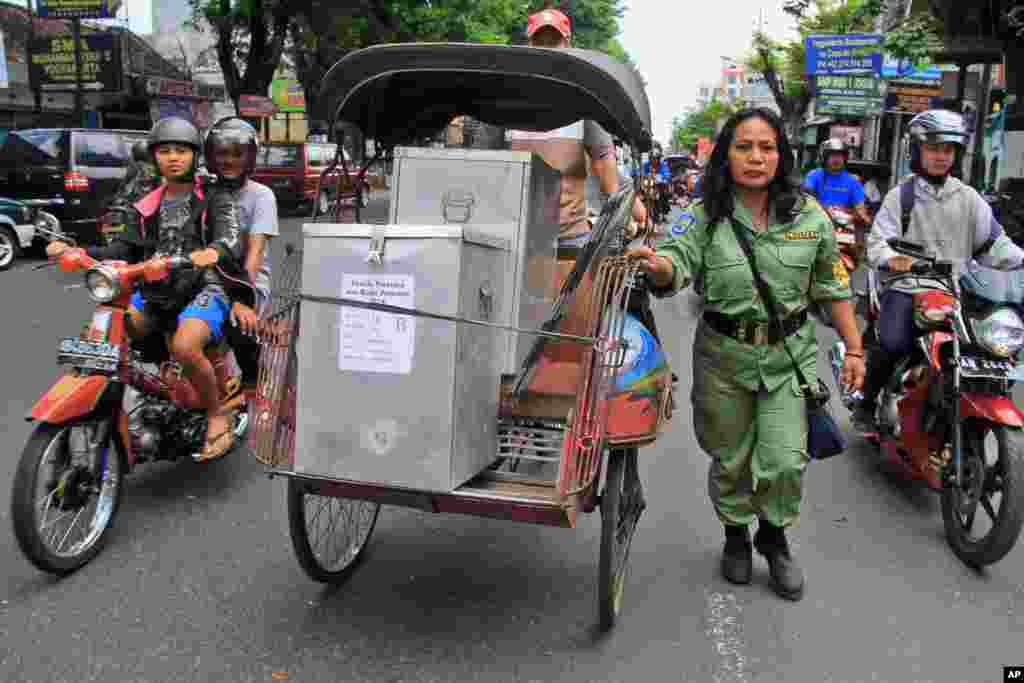 Seorang petugas keamanan mengawal becak yang membawa kotak-kotak berisi kertas suara di Yogyakarta (8/7).&nbsp;(AP/Slamet Riyadi)