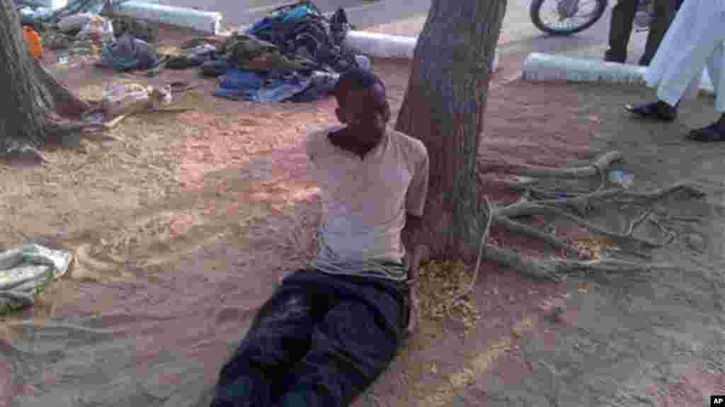 In this photo taken with a mobile phone, Tuesday, May. 7, 2013, Bakura Ibrahim, a suspected member of Islamic extremist group arrested by soldiers is tied to a tree in Bama, Nigeria.