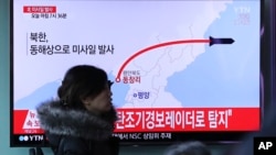 A woman at a train station in Seoul walks by a TV screen showing a news report about North Korea's missile test, March 6, 2017.
