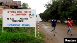 FILE - People jog past a sign with a message by the M23 rebel movement in their campaign against rampant corruption in Rutshuru town in the Democratic Republic of the Congo on Nov. 3, 2012. 