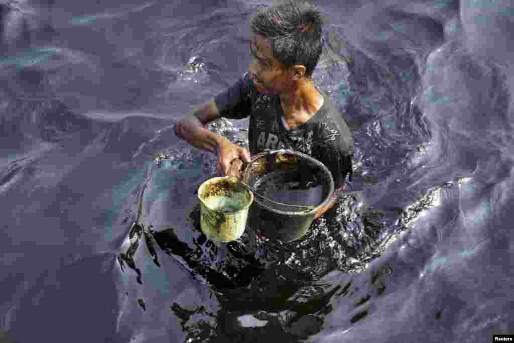 A fisherman collects spilled crude oil at the Pantai Teluk Penyu in Cilacap, Indonesia's Central Java province, May 25, 2015 in this photo taken by Antara Foto. Damage to PT Pertamina crude oil unloading facility at 16 nautical miles south of Cilacap's shore caused 14,000 liters of crude oil to leak and pollute the coastal waters, according to Antara.