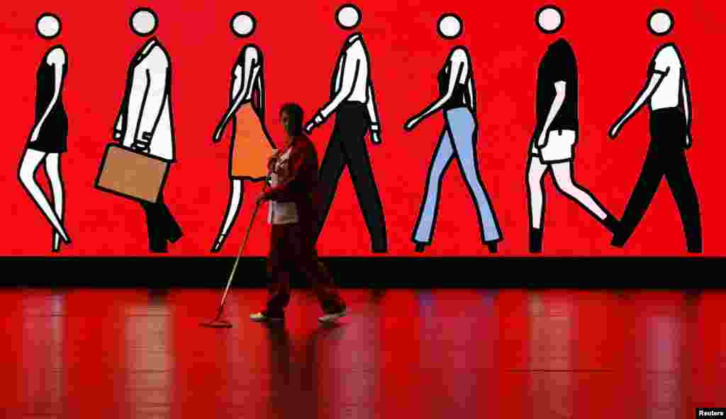 A cleaner sweeps the floor as she walks past an illuminated sign depicting people walking, at Spain&#39;s Santander headquarters in Boadilla del Monte outside Madrid.