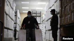 Un soldado vigila mientras un trabajador lleva cajas con materiales de votación para distribuir en todo el país antes de las elecciones generales del 28 de noviembre, en Tegucigalpa, Honduras, el 23 de noviembre de 2021.