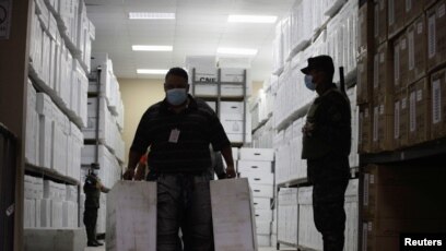Un soldado vigila mientras un trabajador lleva cajas con materiales de votación para distribuir en todo el país antes de las elecciones generales del 28 de noviembre, en Tegucigalpa, Honduras, el 23 de noviembre de 2021.