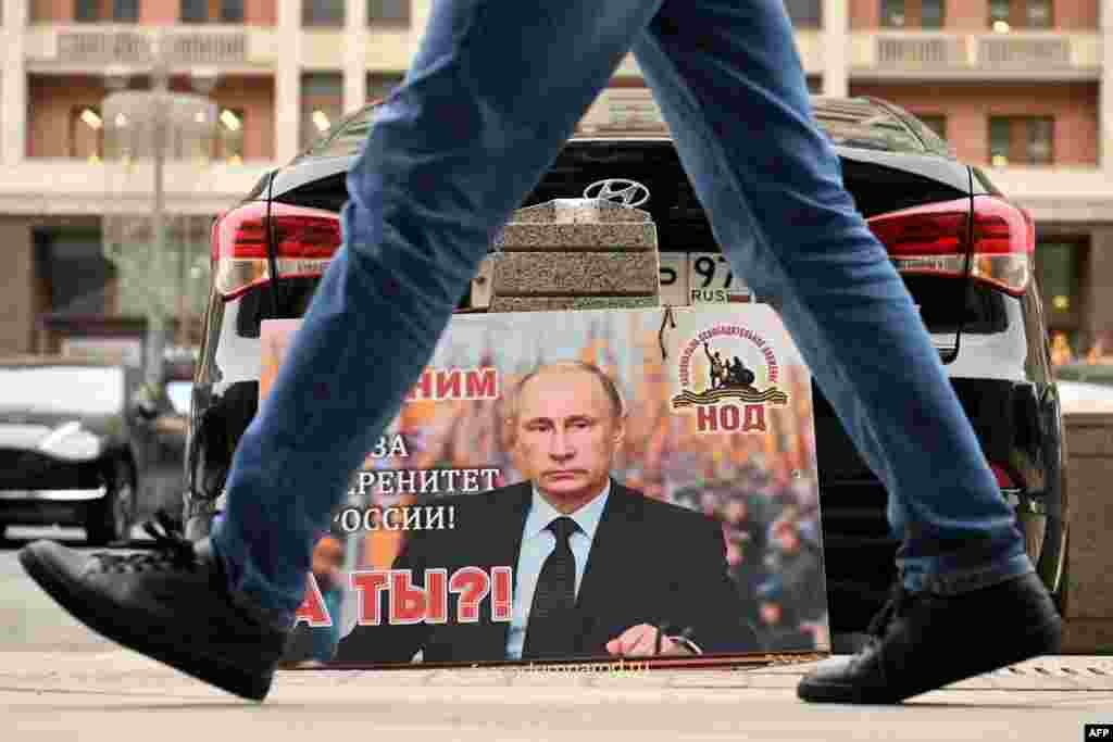 A placard featuring an image of Russian President Vladimir Putin and reading &quot;We are with him for the sovereignty of Russia! And you?&quot; is seen left in front of the Russian State Duma building in central Moscow.