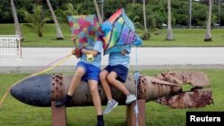 Dua siswa sekolah duduk di atas sebuah torpedo dari Perang Dunia II, yang dipajang di Taman Memorial Asan di Pulau Guam, wilayah AS (11/7). Hari Kamis (17/8), 30 ribu lebih siswa sekolah negeri kembali dibuka setelah libur musim panas. 