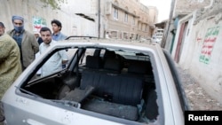 People gather near a car damaged by a bomb explosion outside a house belonging to a Shi'ite Houthi man in Sanaa, Dec. 8, 2014. 