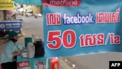 រូបឯកសារ៖ ស្ត្រី​ម្នាក់​លក់​ស៊ីមកាត​ទូរស័ព្ទ​ដៃ​នៅ​ក្បែរ​ផ្ទាំង​បដា​មួយ​ដែល​ផ្សព្វផ្សាយ​ទាក់ទិន​នឹង​ Facebook រាជធានីភ្នំពេញ ថ្ងៃទី២២ ខែមីនា ឆ្នាំ២០១៨។ TANG CHHIN Sothy / AFP 
