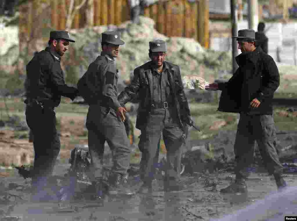 Smoke rises as a firefighter sprays water on the ground while Afghan police inspect the site of a suicide attack in Kabul, Nov. 27, 2014.