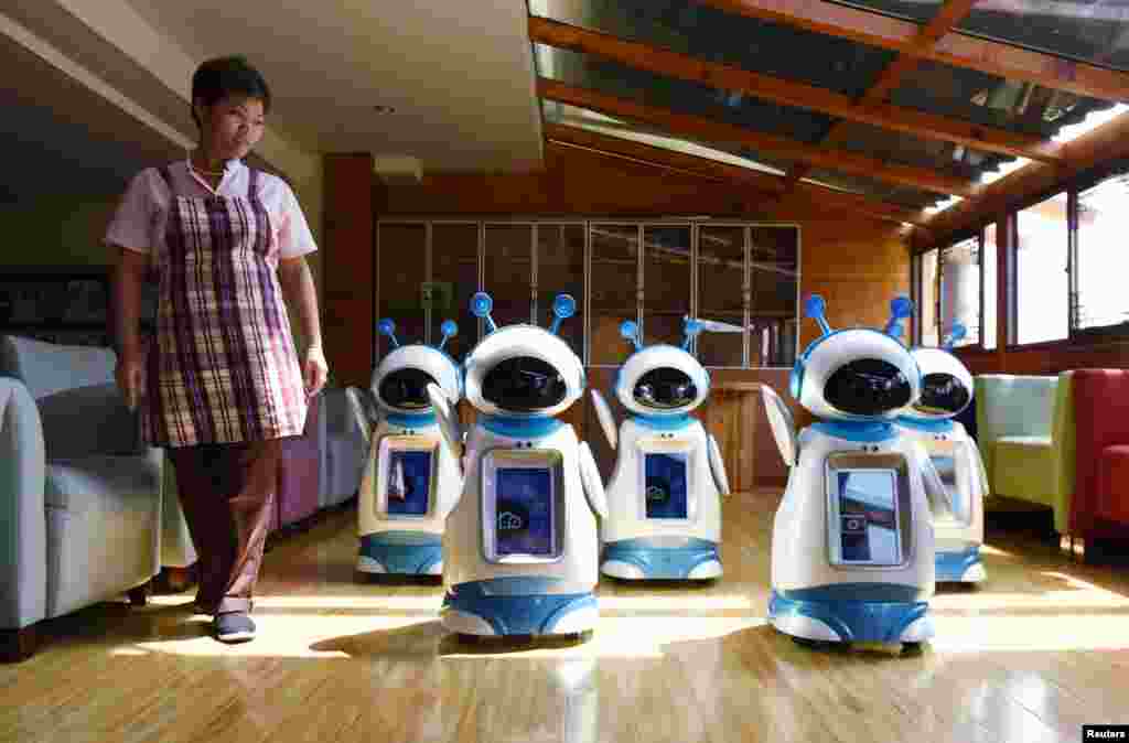 A staff walks past robots serving at a nursery home in Hangzhou, Zhejiang Province, China.