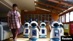 A staff walks past robots serving at a nursery home in Hangzhou, Zhejiang Province, China, May 17, 2016. 