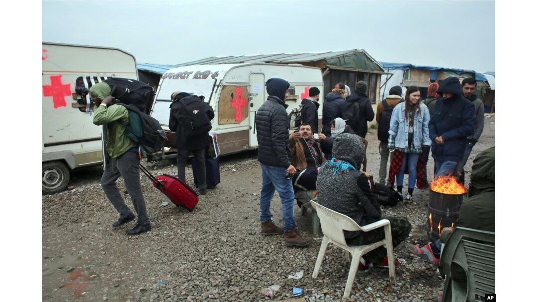 Migrants carrying their belongings walk past other migrants warming themselves around a fire as they leave a makeshift camp known as "the jungle" near Calais, northern France, to register at a processing center, Oct. 24, 2016.