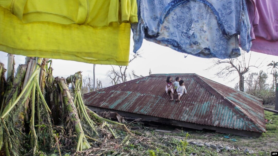 Anak-anak duduk di atas atap rumah yang diterbangkan topan Koppu di kota Casiguran, provinsi Auroran, sebelah timur laut Manila, Filipina (21/10). (AFP/Dante Diosina)