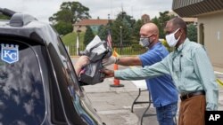 A motorist is handed a bag containing information about open positions at a drive-thru job fair in Omaha, Neb., July 15, 2020. 