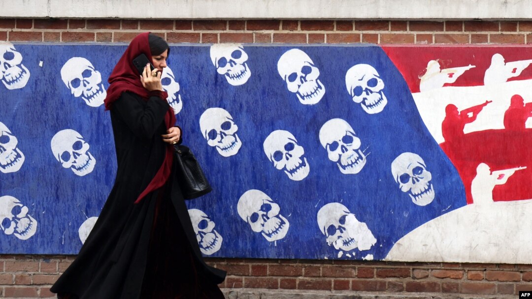 A woman uses her cellphone as she walks past a mural painted on the outer wall of the former US Embassy in Tehran, Iran, dubbed the 'Den of Espionage,' on March 8, 2025.