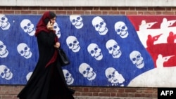 A woman uses her cellphone as she walks past a mural painted on the outer wall of the former US Embassy in Tehran, Iran, dubbed the 'Den of Espionage,' on March 8, 2025.