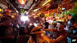 FILE - Patrons enjoy cold tropical cocktails in the tiny interior of the Tiki-Ti bar as it reopens on Sunset Boulevard in Los Angeles.