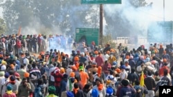 Para petani yang melakukan protes berdiri di balik asap yang diakibatkan gas air mata di dekat perbatasan Shambhu yang memisahkan negara bagian Punjab utara dan Haryana, hampir 200 km dari New Delhi, India, 14 Februari 2024. (Foto: AP)