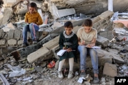 Anak-anak menulis di buku catatan di dekat reruntuhan bangunan yang hancur di dekat tenda yang digunakan sebagai pusat pendidikan sementara bagi siswa sekolah dasar di Jabalia di Jalur Gaza utara pada 8 September 2024. (Foto: AFP)