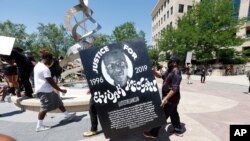 FILE - Demonstrators carry a giant placard during a rally and march over the death of 23-year-old Elijah McClain outside the police department in Aurora, Colo., June 27, 2020.