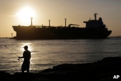 Sebuah kapal tanker minyak melewati seorang nelayan saat memasuki sebuah kanal dekat Port Aransas, Texas, menuju Pelabuhan Corpus Christi. (Foto: AP)